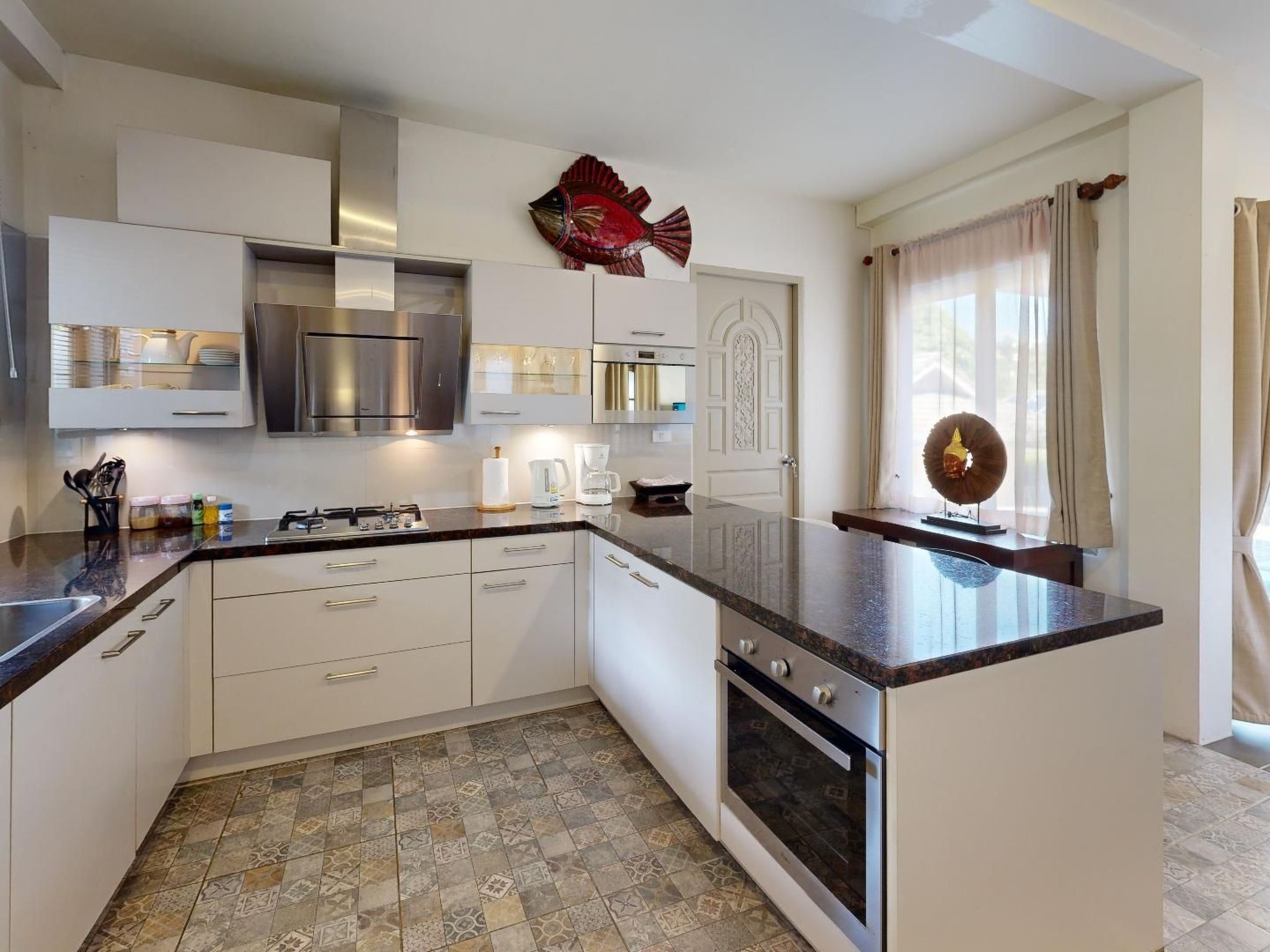 A modern kitchen with white cabinets, a stainless steel range hood, a built-in oven, and a large island with a dark countertop.