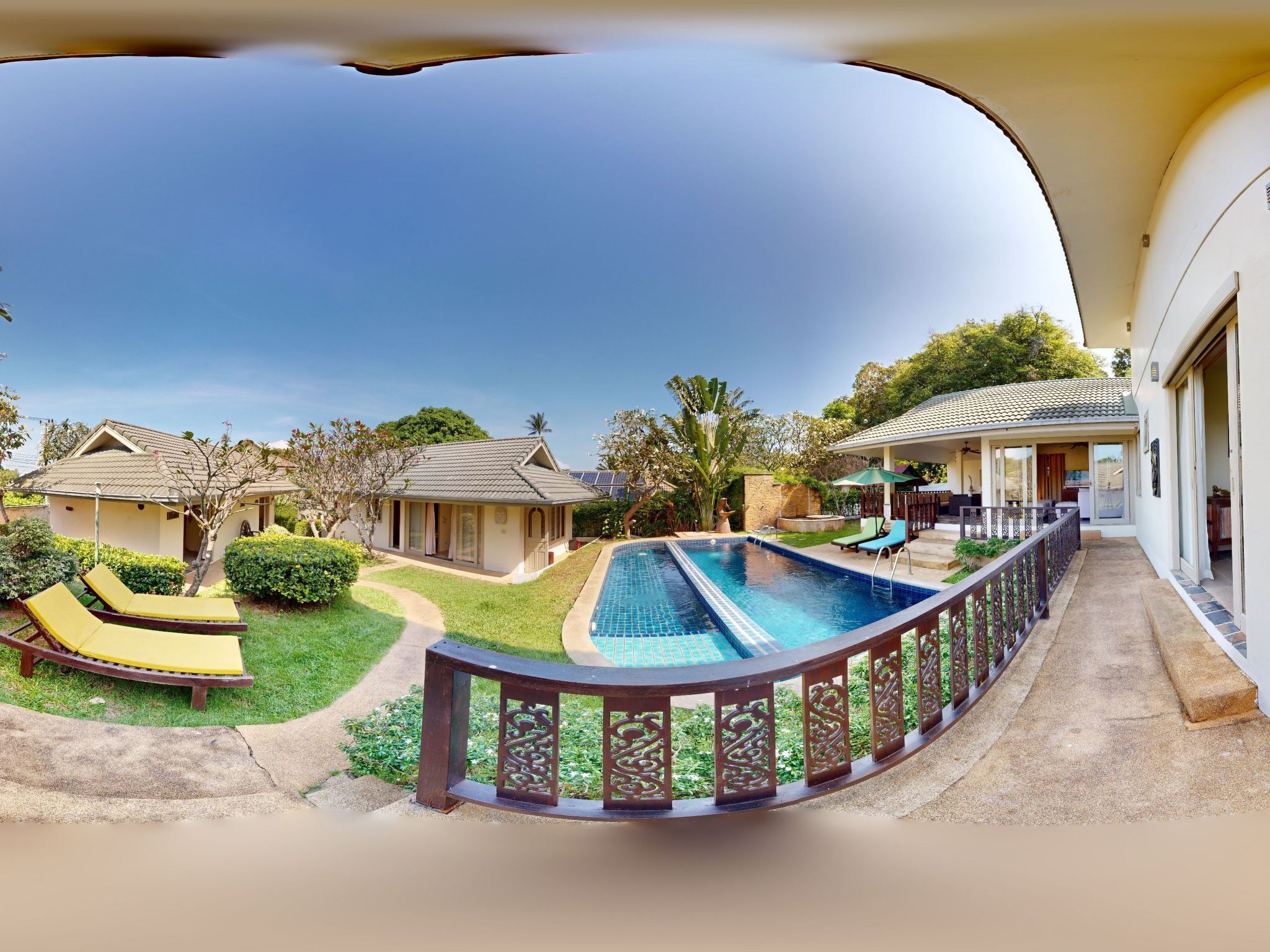 A pool area with a curved wooden railing, a lounge chair, and a small house with a tiled roof.