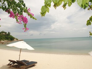 A beach with a white umbrella and two wooden lounge chairs. - Villa mit Blick auf das Wasser by Interhome (Koh Samui)