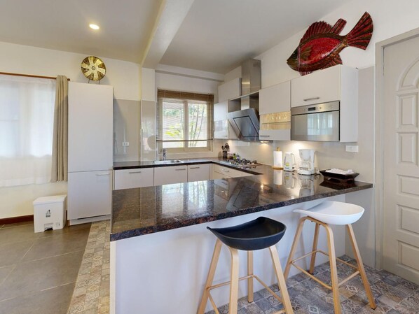 A modern kitchen with a central island, bar stools, and a decorative fish wall art piece. - Villa mit Blick auf das Wasser by Interhome (Koh Samui)