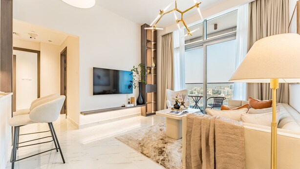 A modern living room with a sofa, a coffee table, a TV, and a city view. - Community View 1BR, Perfectly Located Near the Park, Adhara Star, Arjan (Dubai)