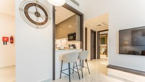 A modern kitchen with a microwave, a bar area with two stools, and a large abstract painting on the wall. - Community View 1BR, Perfectly Located Near the Park, Adhara Star, Arjan (Dubai)