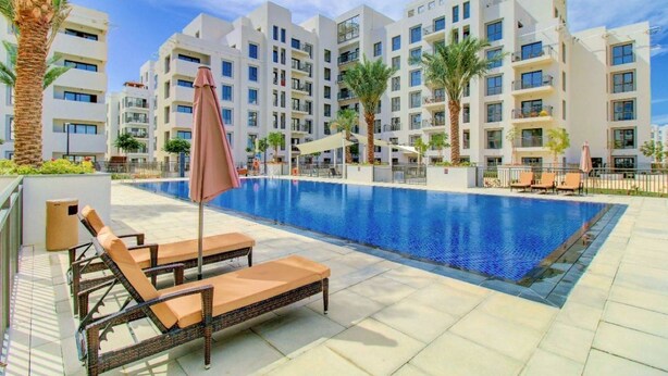 Un hotel moderno con una grande piscina, lettini prendisole e palme.