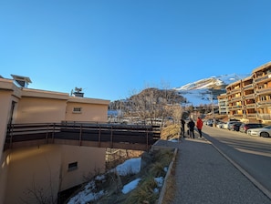 Ein Wohngebiet mit einem gepflasterten Weg, einer kleinen Brücke und Gebäuden mit Balkonen mit Blick auf einen verschneiten Berg.