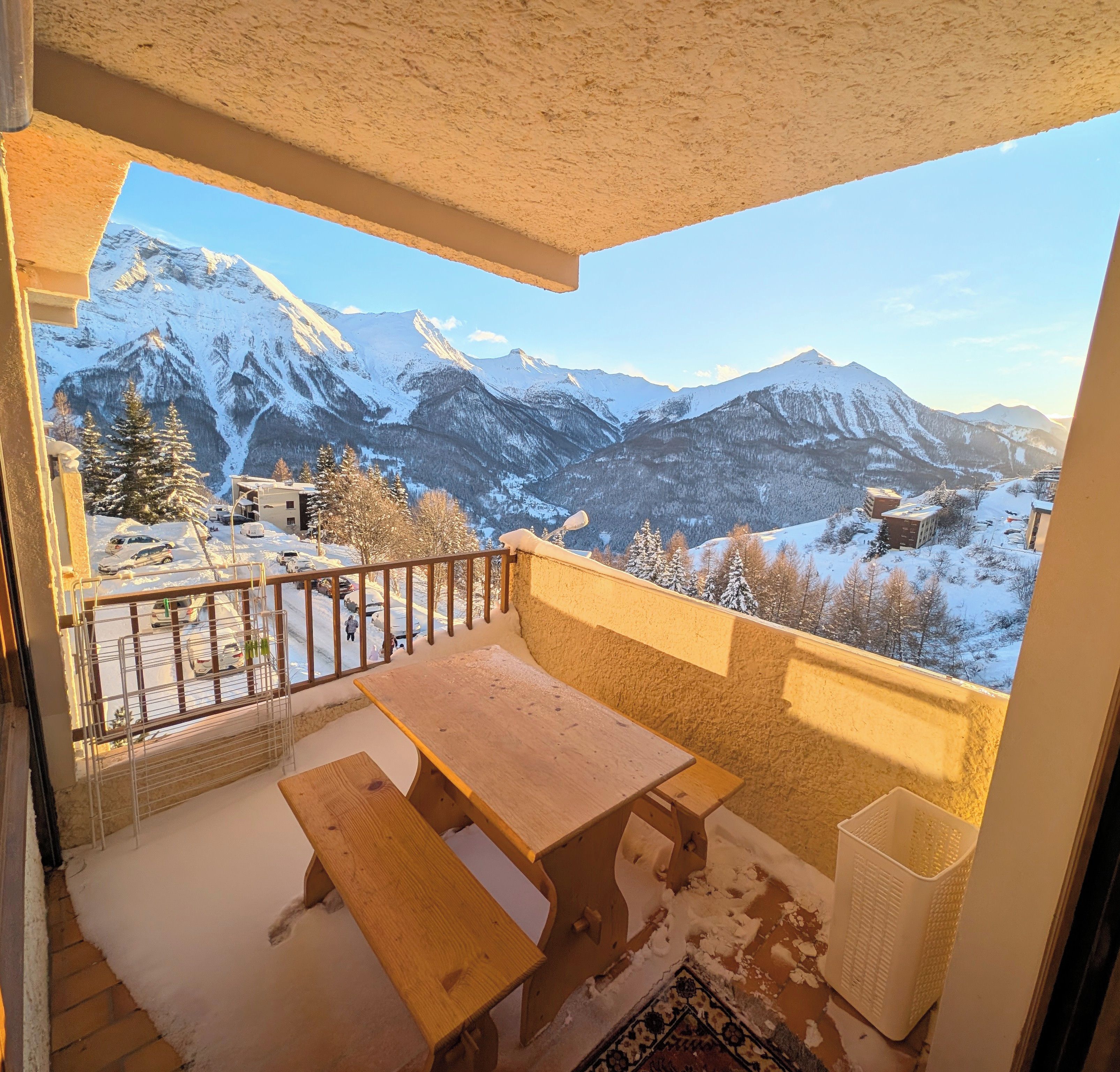 A balcony with a wooden table and benches, overlooking a snowy mountain landscape.