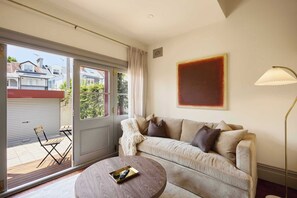 A living room with a sofa, a coffee table, a lamp, and a sliding glass door leading to an outdoor area. - Four-Bedroom Heritage Terrace in Paddington (Paddington)