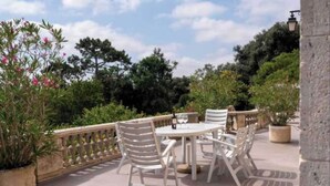 An outdoor patio with a round table and white chairs, surrounded by greenery and a stone balustrade. - Stay at the Château- Studio 2P- with pool and park (Fajolles)