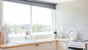 Une cuisine avec une fenêtre, un évier, une cuisinière et une bouilloire.