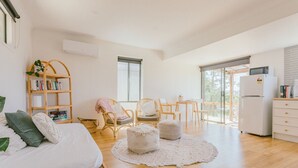 Un vaste espace de vie comprenant un canapé, des poufs, une bibliothèque en bois, une table à manger et un réfrigérateur.