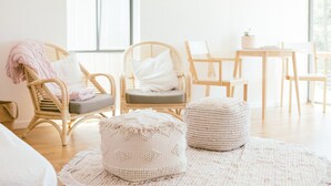 Une pièce lumineuse et aérée, meublée de meubles en osier, avec un pouf rond et une petite table sur laquelle est posée une plante.