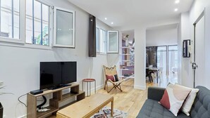 A modern living room with a flat-screen TV, wooden entertainment unit, a grey sofa, and a dining area in the background.