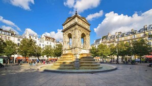A historic fountain with a central structure surrounded by a circular plaza, with buildings in the background.