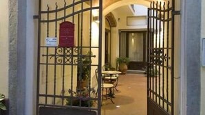 Ein Gebäude mit einem bogenförmigen Eingang, einem schmiedeeisernen Tor, einem roten Schild und einem Innenhof mit Tisch und Stühlen.