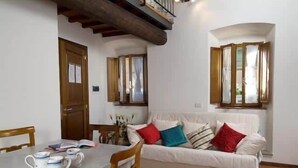 Ein gemütliches Wohnzimmer mit einem weißen Sofa, einem Holzesstisch und einem Fenster mit Vorhängen.