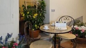 Eine Terrasse im Freien mit einem runden Tisch, zwei Stühlen, einem Blumentopf und einer Wandleuchte.