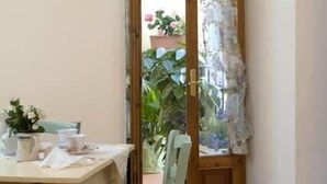 Un comedor con una mesa preparada para dos, una silla y una puerta que da a un jardín.