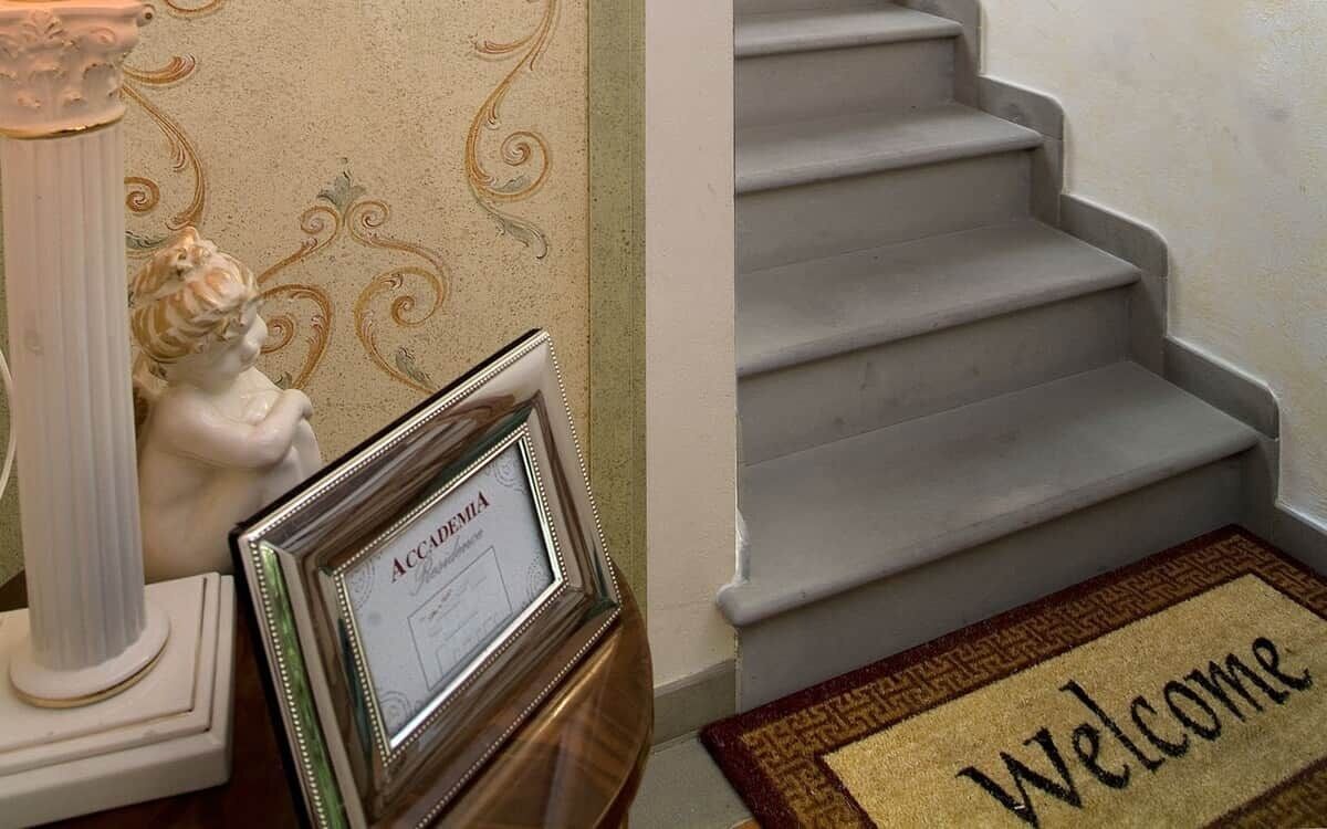 A staircase with a welcome mat and a framed diploma on a table.