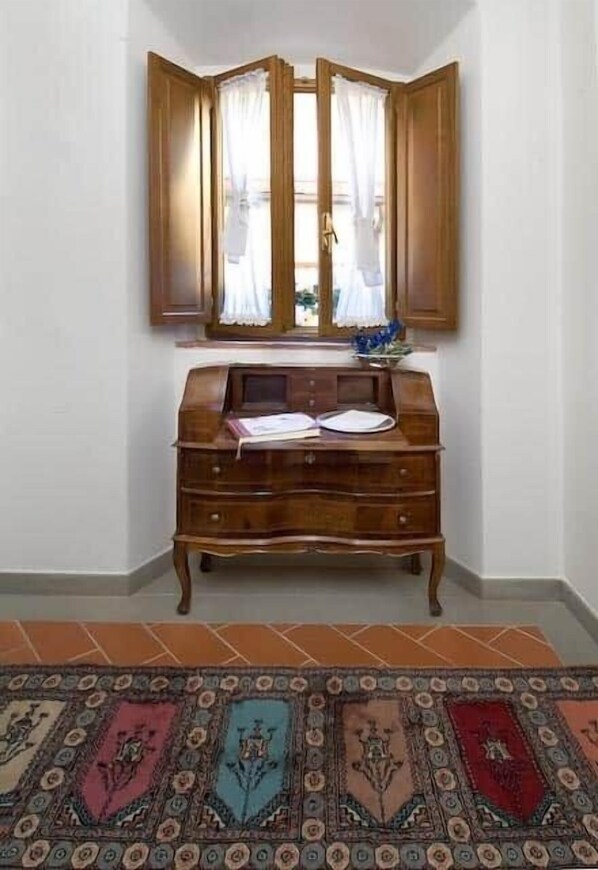 Habitació d'angle amb escriptori de fusta, finestra amb cortines i una catifes amb dibuixos.