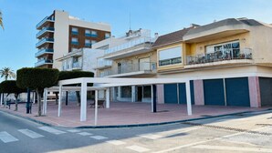 A multi-story building with balconies, a covered outdoor seating area, and a street view.