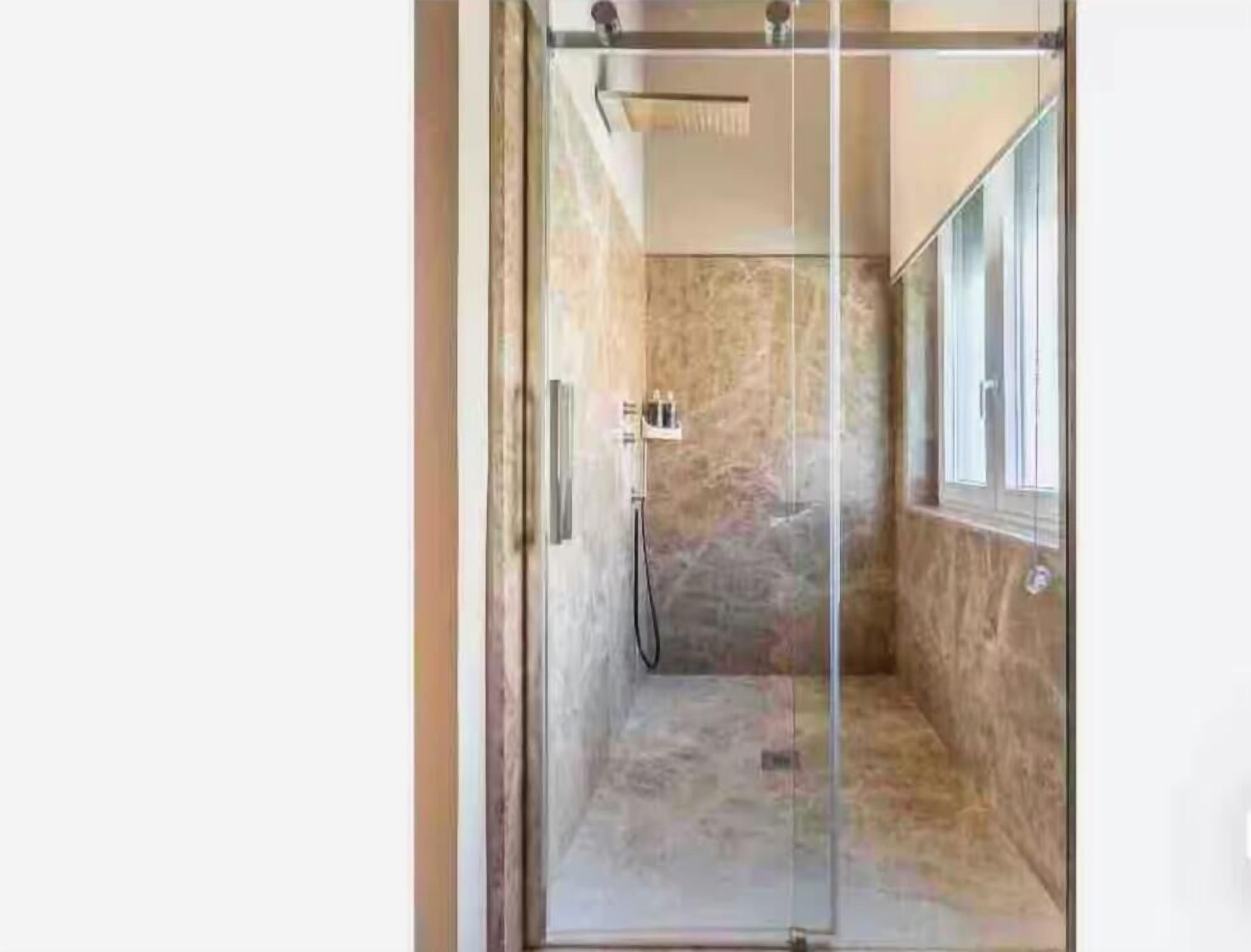 Une douche fermée par des parois de verre, avec un mur en marbre et une fenêtre.