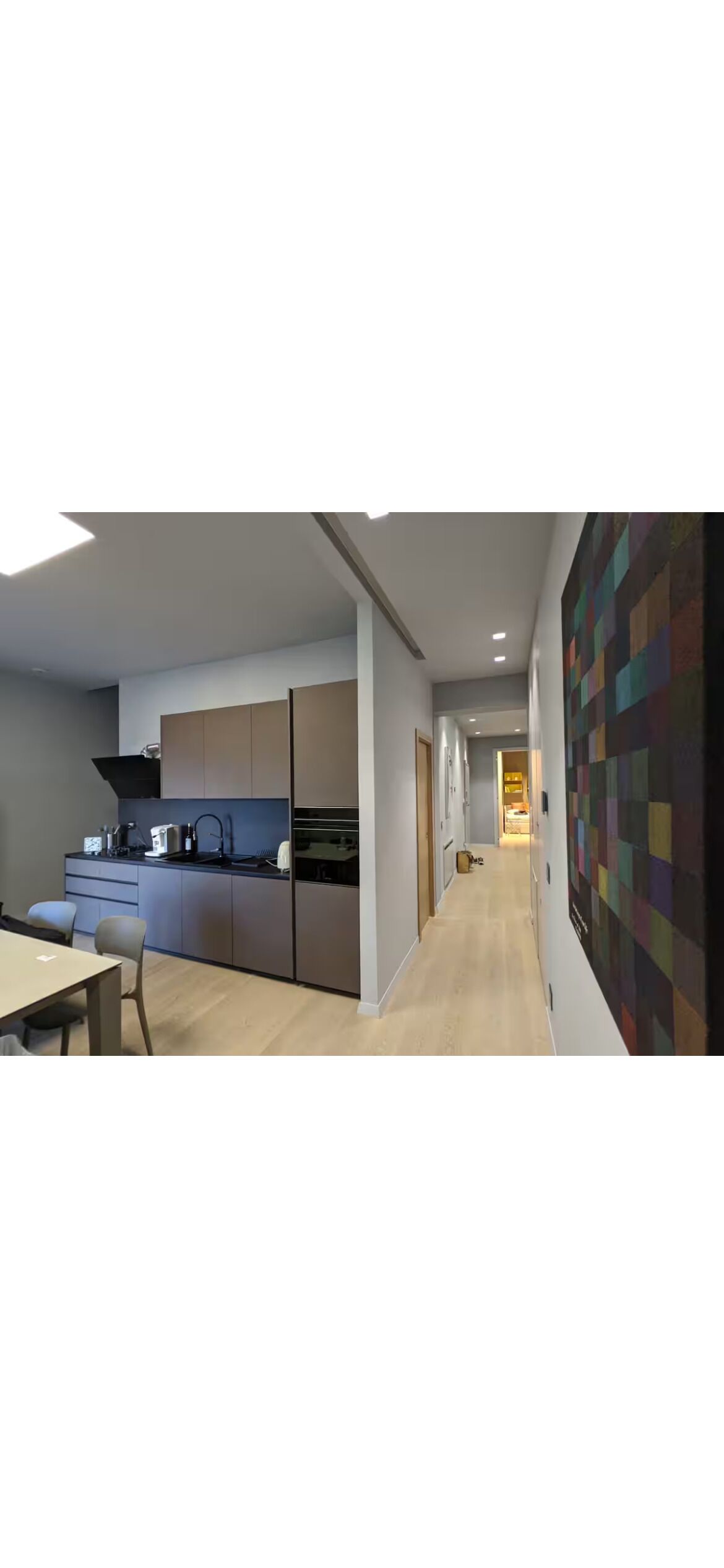 Une cuisine moderne dotée d’un îlot central, d’un coin repas avec une table et des chaises, et d’un mur décoré d’une œuvre abstraite aux couleurs vives.