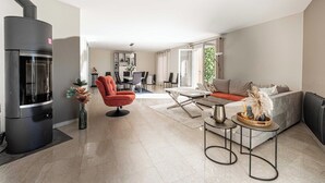 A modern living room with a fireplace, a sofa, a coffee table, and a dining area in the background. - Quiet House with Pool (Biot)