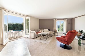 Uma sala de estar ampla com sofá, uma poltrona vermelha, mesa de centro e conjunto de jantar.