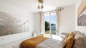 A bedroom with a bed, a large window, a view of greenery, and a rope bridge artwork on the wall. - Quiet House with Pool (Biot)