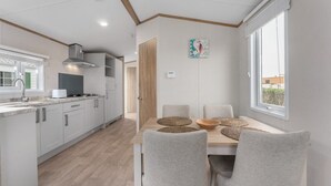 Une cuisine moderne avec des meubles blancs, une table à manger en bois et une vue sur l’extérieur grâce à une grande fenêtre.