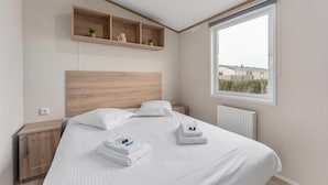 Une chambre d’hôtel moderne avec une tête de lit en bois, une grande fenêtre offrant une belle vue et une étagère intégrée agrémentée d’objets décoratifs.