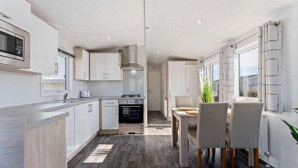 A modern kitchen with white cabinets, a built-in oven, and a dining area with a table and chairs.