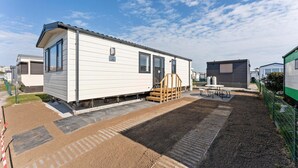 A mobile home with a covered patio area, a small outdoor table, and a wooden staircase leading to the entrance.
