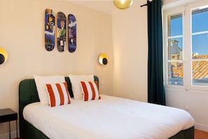 Een bed met witte beddengoed en gestreepte kussens, een groen hoofdeinde en een muur met drie skateboards.