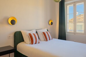 Una cama con almohadas a rayas blancas y naranjas, cabecera verde y dos lámparas fijadas a la pared.