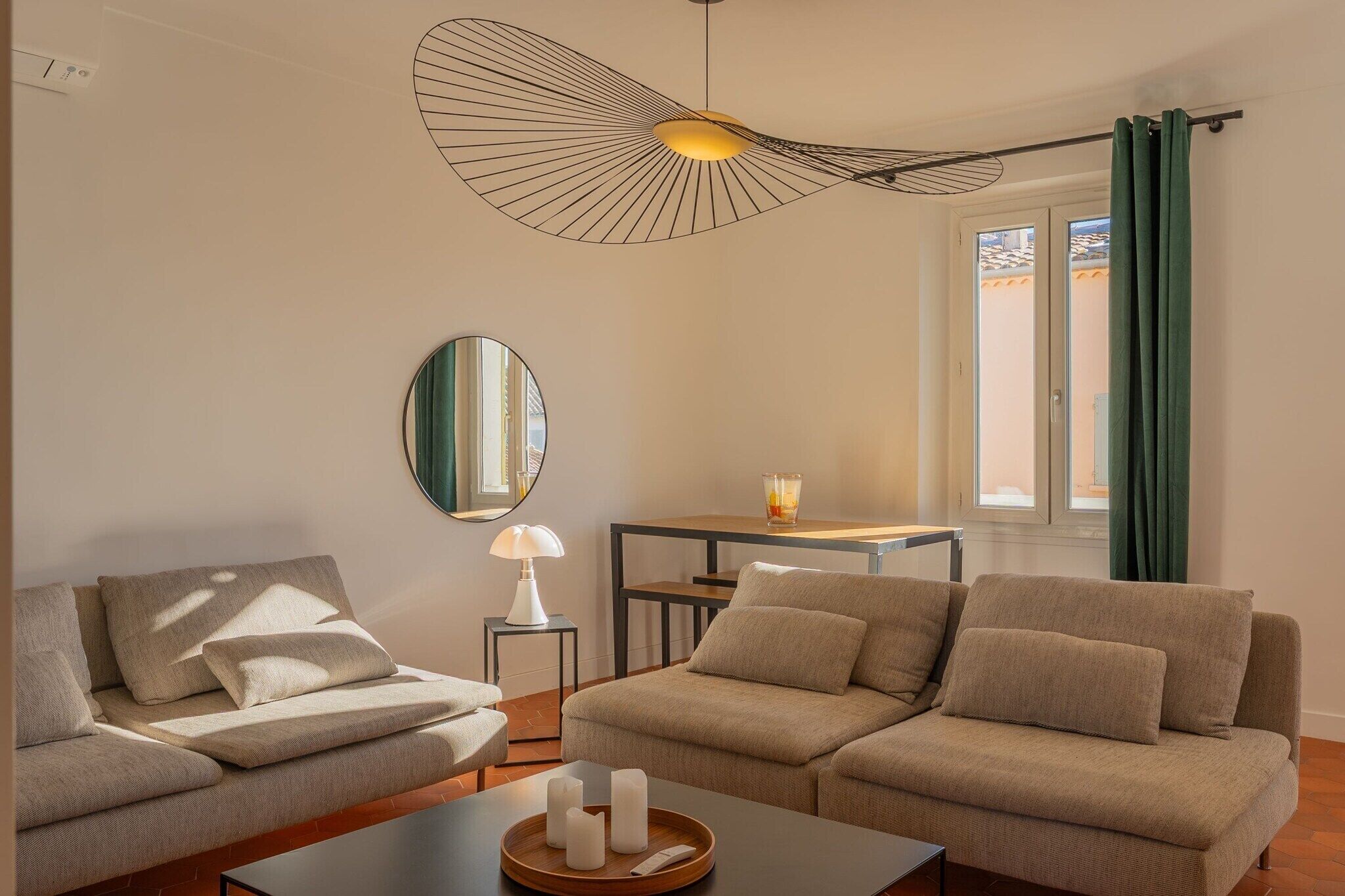 Un soggiorno moderno con un divano, un tavolino da caffè con candele, una lampada, uno specchio e un lampadario originale.