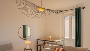 Ein Wohnzimmer mit einer Couch, einem Tisch, einer Lampe, einem Spiegel und einem Fenster mit Vorhängen.