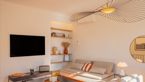 A modern living room with a flat-screen TV, a sofa, a coffee table, and a unique ceiling light fixture. - Saint-Tropez: Bright apartment near the port (Saint-Tropez)