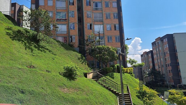 Ein mehrgeschossiges Wohngebäude mit Balkonen, einer Treppe, die zu den oberen Stockwerken führt, und einer sanften Grasfläche.