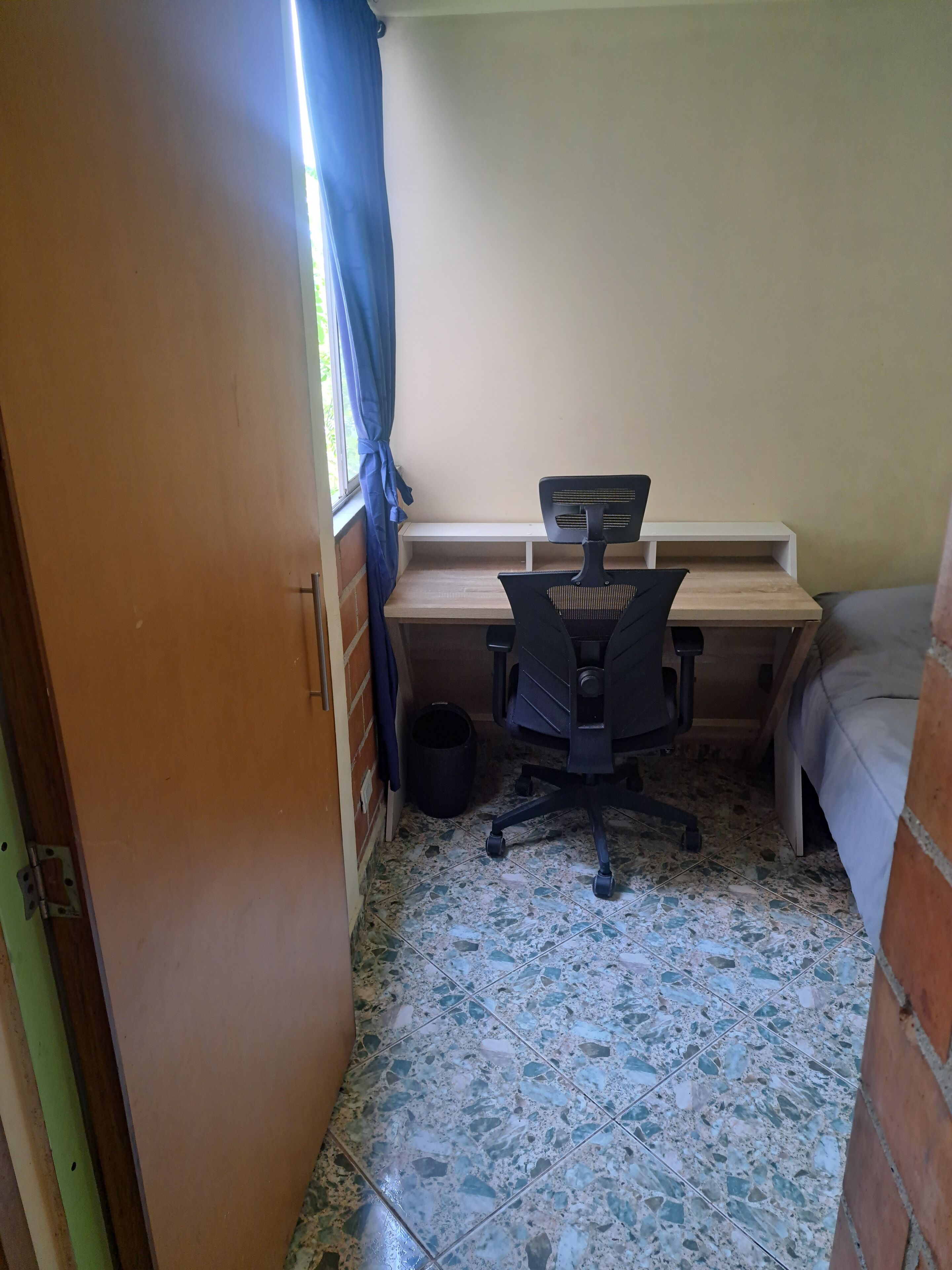 Una habitación pequeña con escritorio, silla y cama.