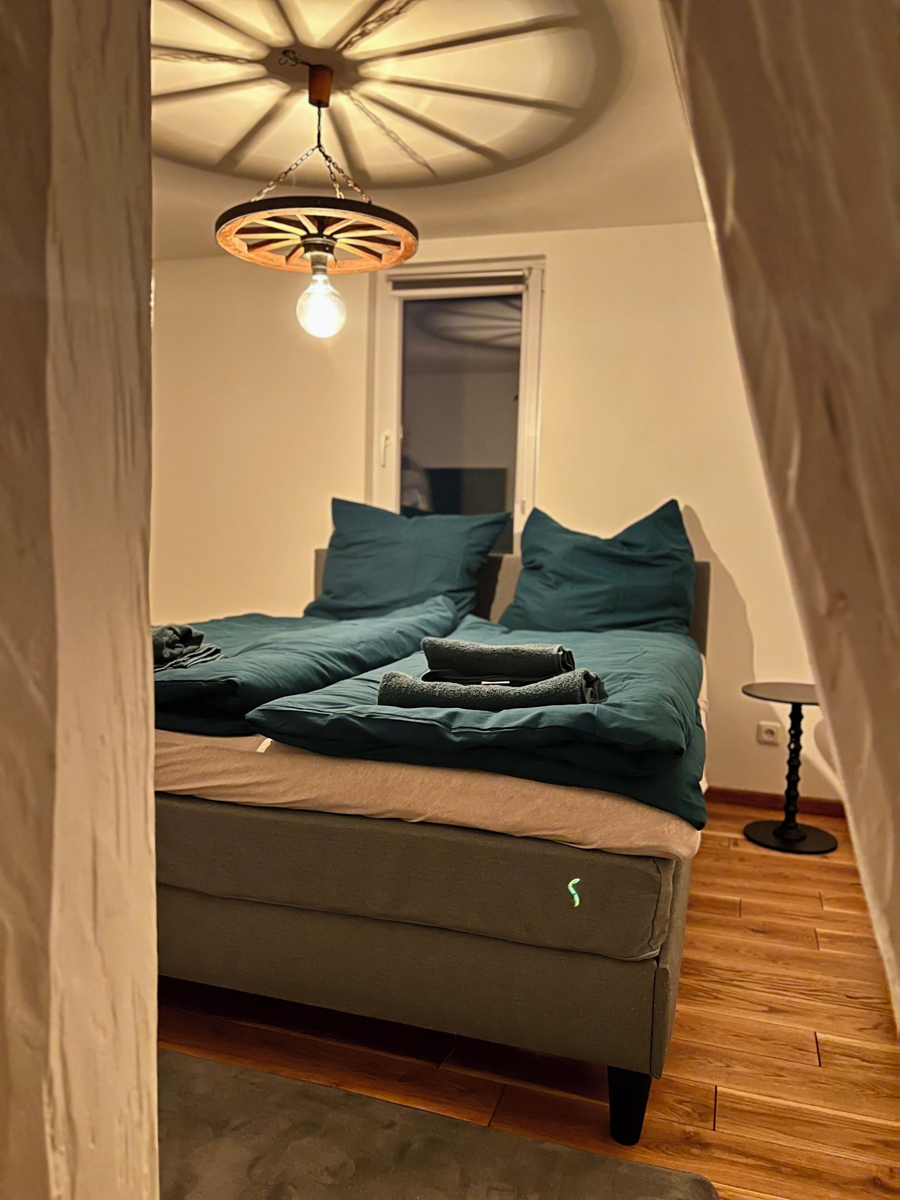 A cozy bedroom with a bed, pillows, a bedside table, and a unique ceiling light fixture.