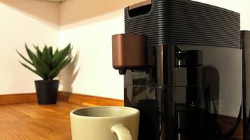 A coffee maker on a wooden table with a white mug beside it.