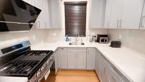 A modern kitchen with white cabinets, a stainless steel stove, a sink, and a window with blinds. - Lovely 3-bedroom house with AC in charming San Gabriel (San Gabriel)