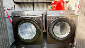 Two front-loading washing machines in a compact space with metal shelving above. - Lovely 3-bedroom house with AC in charming San Gabriel (San Gabriel)