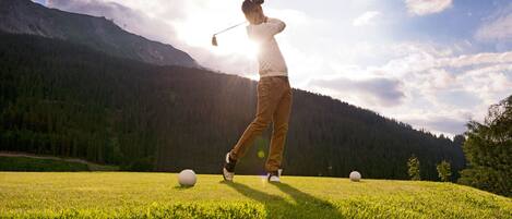 A person playing golf on a grassy field with mountains in the background.