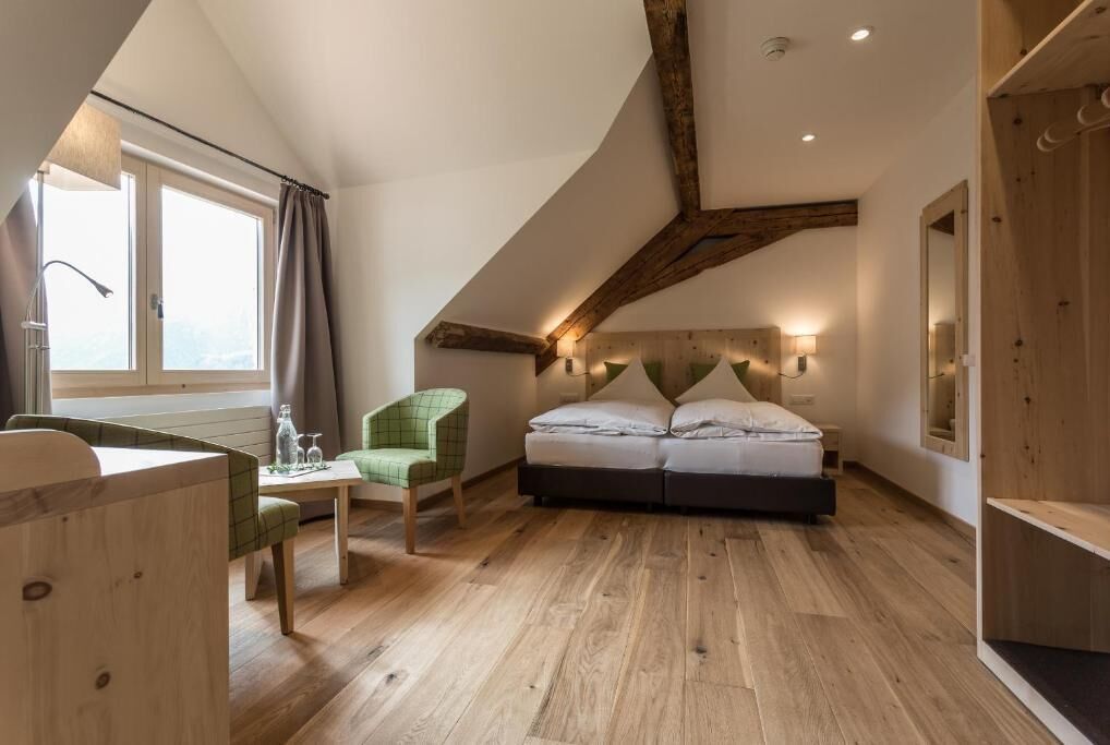 Un dormitorio con techo inclinado, una cama, una silla, una mesa y una ventana con cortinas.