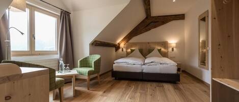 Un dormitorio con techo inclinado, una cama, una silla, una mesa y una ventana con cortinas.