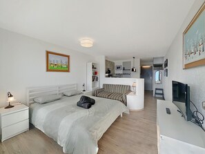 A modern hotel room with a bed, bedside table, lamp, and a TV. - Alpine Club Retreat - Central Studio, Pool & View (Crans-Montana)