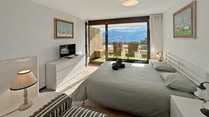 Un dormitorio con cama, televisor, escritorio y ventana con vista a la montaña.