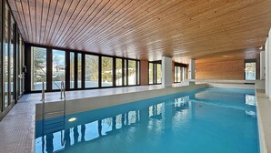 Una piscina interior con techo de madera y ventanas amplias.