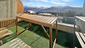Un balcón con mesa y sillas de madera, vista a montañas nevadas y cielo despejado.